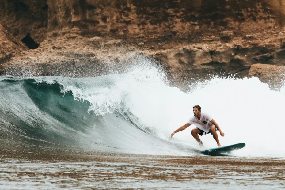 Surfer rides a powerful wave near a rocky coast, capturing the thrill of summer ocean sports.